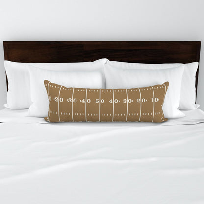 Stadium Stripes gold football lumbar pillow styled on a bed — gold lumbar pillow cover on white bedding with dark wood headboard