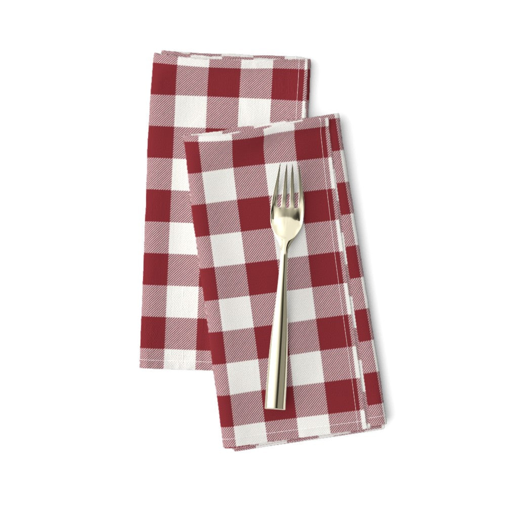 Two red buffalo check cloth napkins folded and offset with a gold fork on top