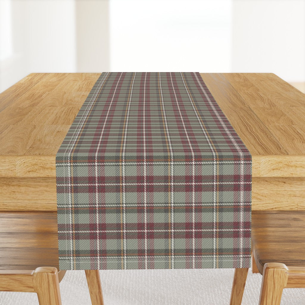 Homestead Plaid table runner in Holiday Berry, a cranberry and sage plaid, hanging off the end of a wood dining table