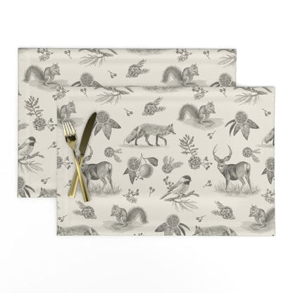 Set of two Woodland Toile placemats in Charcoal with a knife and fork, showing deer, fox and chickadees
