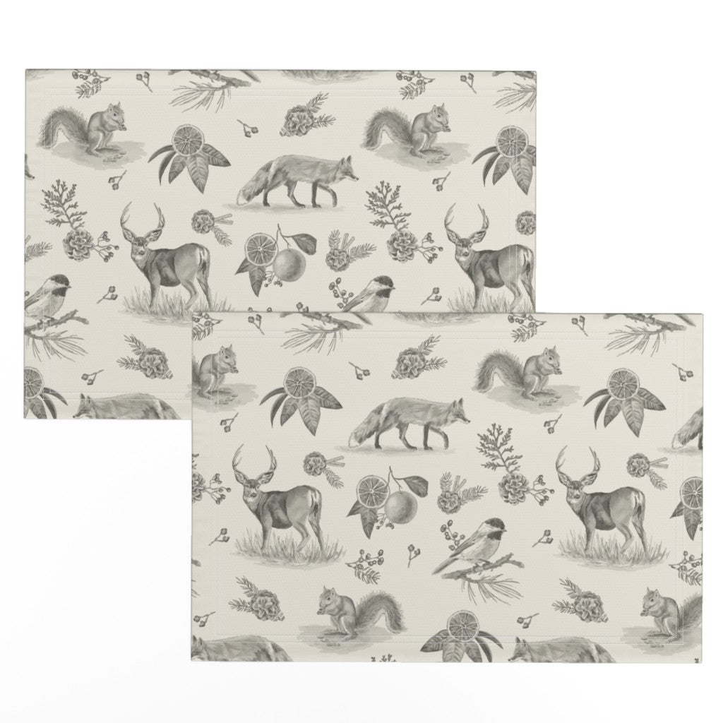 Two charcoal toile placemats offset to show the hand-drawn deer, fox and squirrel