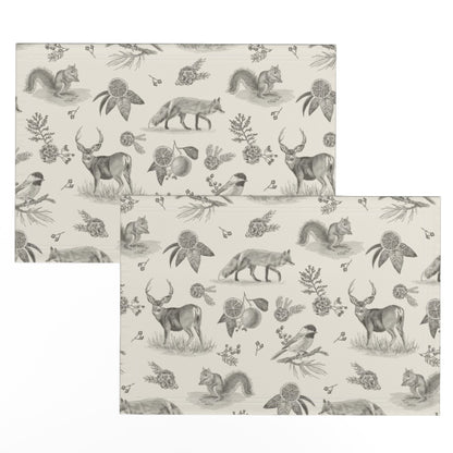 Two charcoal toile placemats offset to show the hand-drawn deer, fox and squirrel